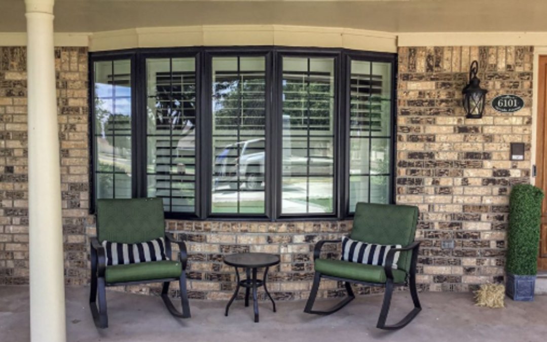 A porch with patio furniture and big, black bow windows.