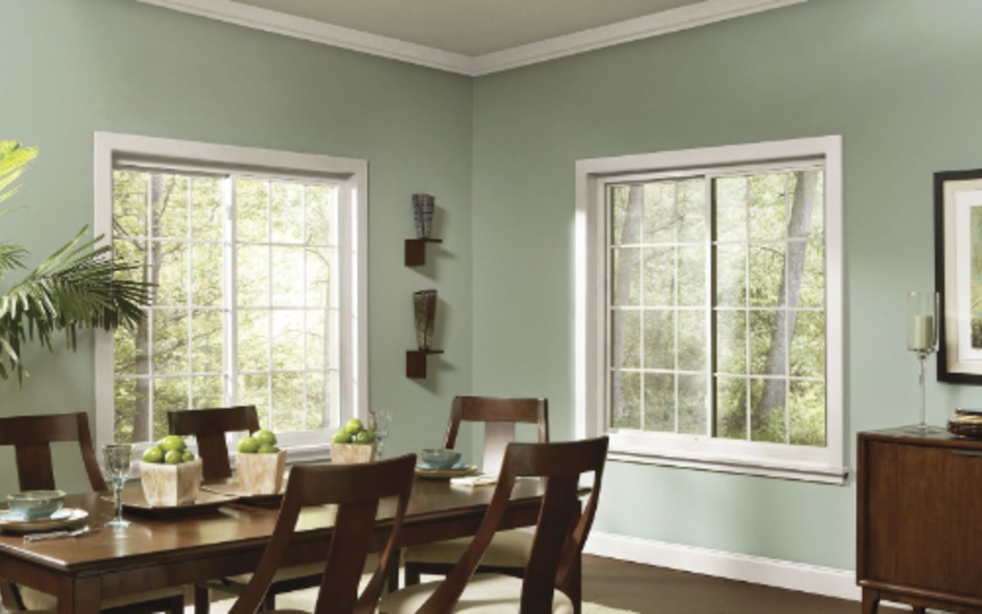 Bright dining room with two large white-framed windows overlooking trees, filling the space with natural light.
